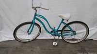 Left side view of Schwinn S1 cruiser bike showing teal frame, white seat, and white handle grips
