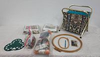Overview of all knitting, needlepoint, and crochet items including metal-framed basket, yarns, needles, needlepoint kits, embroidery hoops and needle gauge.
