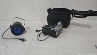 Photo showing the blue tinted flood lamp with metal handle and power cord, vintage Sony Handycam Digital8 camcorder with cables, and black soft carrying case.