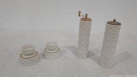 Full set showing two candlestick holders, pepper mill, and salt shaker with embossed white pattern and gold accents
