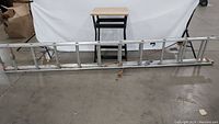Photo of a 20ft metal extension ladder on the floor with a work table in the background