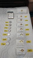 Full lot arranged on white surface showing seven silver dollars with year labels, seven Franklin Mint coins in plastic holders, and a small gold-tone pendant in box.