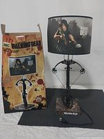 Walking Dead themed table lamp with crossbow base, plug and power cord shown next to original branded box with blood splatter design.