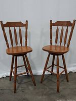 Two wooden swivel bar stools with back support, positioned side by side showing front and side views.