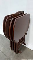 Four dark wood folding TV trays stacked together showing the tray tops and frame in a folded position.