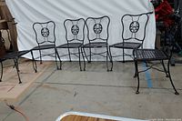 Front view of six black wrought iron patio chairs lined up showing decorative backs and lattice seats.