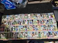 Two photos showing approximately 100 1976 Topps baseball cards laid out on a table, showing fronts with player images, names and teams.