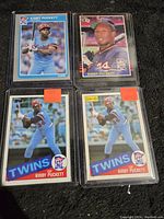 Four Kirby Puckett 1985 rookie cards displayed together on black surface in protective sleeves, showing different card designs and poses.