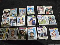 Batch of 1977 Topps baseball cards displayed on dark surface showing mix of teams and players.
