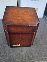 Closed wooden card holder showing deep brown polished wood and brass card suit emblem at base