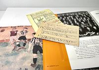 Photo showing an inside page of the book with replicas of handwritten papers, childhood report cards, and a black-and-white photo of a school group.