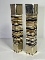 Front view of two tall onyx and alpaca metal candlesticks showing layered banded stone and shiny metal bases