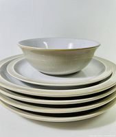 Stack of four cream-colored dinner plates with linen texture and gold rim with a cereal bowl on top
