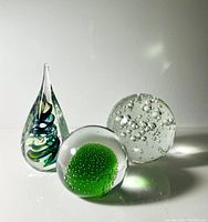 Set of three glass paperweights on white surface showing details of color, bubbles, and shape.