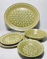 Front view of four dishes showing oval platter, plates, and bowls with green leaf pattern.