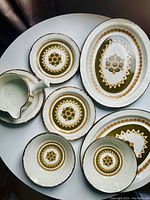 Top-down view of plates, bowls and a small jug showing green and brown floral geometric pattern with visible utensil wear on edges.