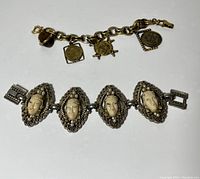 Two bracelets shown side by side on white background, one with carved faces and one with coin charms, all metal with wear.