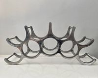 Front view displaying sculptural cast aluminum wine rack with circular spaces for 9 bottles and artistic curved supports.