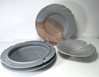Set of three studio pottery plates arranged standing and flat, showing front surfaces and detailed carving.