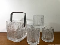 Full shot of ice bucket with metal handle beside four old fashioned glasses, all with textured Hoya5 pattern.