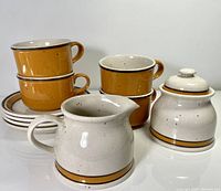 Photo showing 3 cups stacked, 1 cup next to creamer jug and lidded sugar bowl, with 4 saucers underneath cups