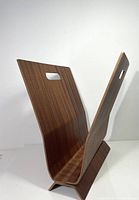 Angled front view of vintage bentwood magazine rack showing curved wood panels and handle cutouts.