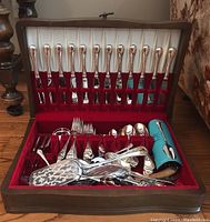Open wooden chest lined with red velvet containing Birks Regency Plate flatware and serving utensils
