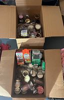 Top-down photo showing two open boxes filled with assorted glass canning jars and multiple packages of lids, some lids are loose and some in packaging.