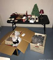 Christmas decorations on black folding table and boxes with items on basement floor
