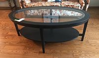 Oval IKEA MALMSTA coffee table with wood veneer frame and tempered glass top shown from side angle on wood floor.