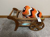 Wooden doll cart with two blankets (one crocheted orange, white, brown) on top plus a brown shrug.