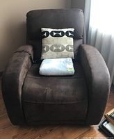 Front view of brown electric recliner with beige and black patterned cushion and gray throw on seat, wired remote visible on armrest.