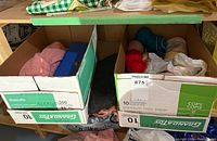 Photo showing two cardboard boxes on a shelf containing yarn skeins and sewing accessories