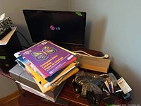 LG monitor powered on showing LG logo, various office supplies like colorful construction paper, and cables on table.