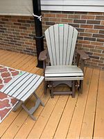 Front view of rocker chair and side table on deck with brick wall background