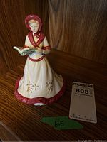 Front view of the figurine showing a woman in cream and red dress holding an open book.