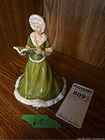 Image showing the full front and side view of the Royal Doulton figurine depicting a woman dressed in green with white bonnet and holding a book.