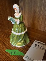 Front view of the Royal Doulton figurine showing a woman in a green dress holding a book, placed on a wooden surface with a green arrow sign indicating 6.5 inch height.
