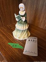 Figurine front side showing woman holding a book, dress with floral details.