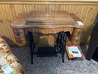Front view of antique wooden seamstress sewing cabinet with wrought iron treadle, showing four drawers with decorative metal pulls and the top closed.
