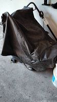 Snowblower covered by a black protective cover showing wheels and handle bar.