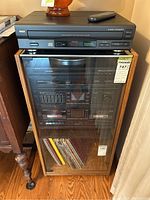 Overall stereo system inside laminate wood and glass cabinet, showing RCA CD changer on top.