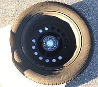 Single tire and rim assembly laid flat on concrete showing wheel center and tire sidewall.