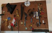 Wide view of pegboard with assorted hand tools hanging including wrenches, screwdrivers, hand saw, hatchet, clock, and other items.