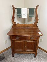 Front view of wooden wash stand with dovetail drawer, cupboard, and decorative towel rail with towels.
