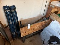Folded wooden top work mate with metal base, positioned against wall, next to two blue metal folding sawhorses.