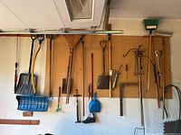 Wide shot of yard tools hanging on pegboard including shovels, rakes, cultivator, dustpan, and bike pump