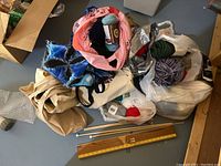 Full view of multiple bags containing yarn skeins and knitting supplies including needles and measuring board