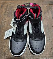 Front view of the pair of high-top kids shoes showing toe area and black, white, red colors with laces and Velcro strap.