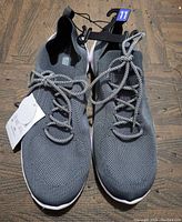 Pair of men's gray knit athletic shoes size 11 with white soles and reflective laces on wooden floor.